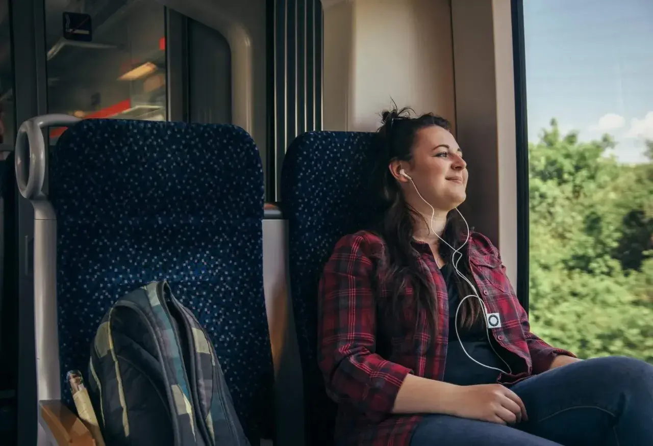 Ung kvinna lyssnar på musik i hörlurar under en resa med biltåg genom Europa.