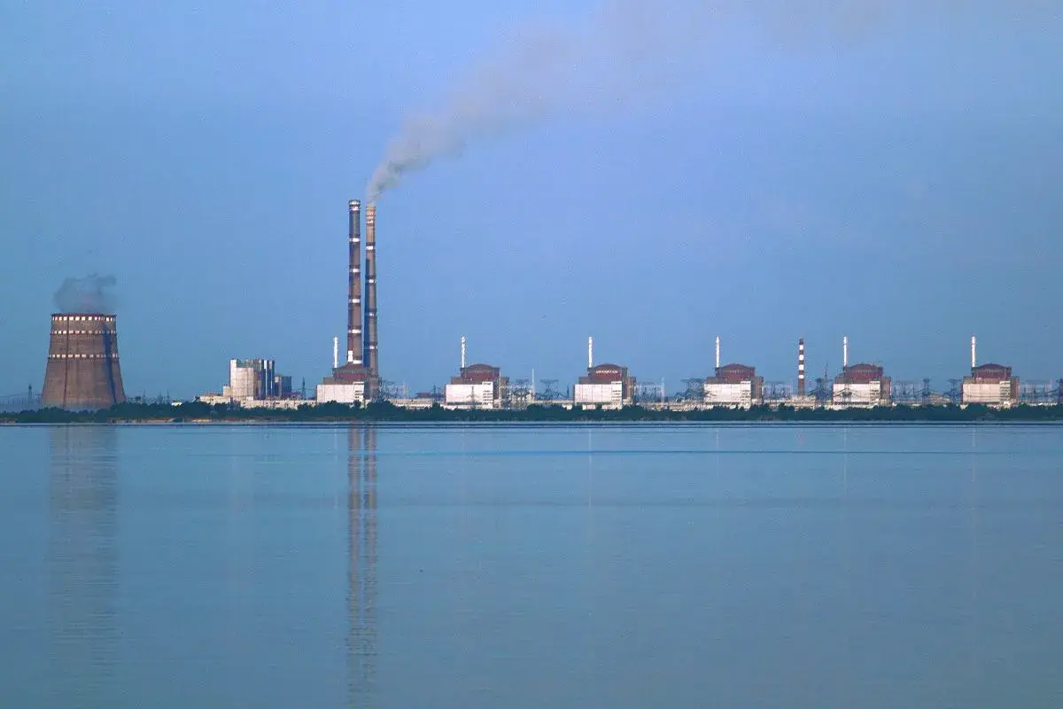 Zaporoże: potężna elektrownia atomowa z chłodnią kominową i dymiącymi kominami, na tle spokojnej wody.