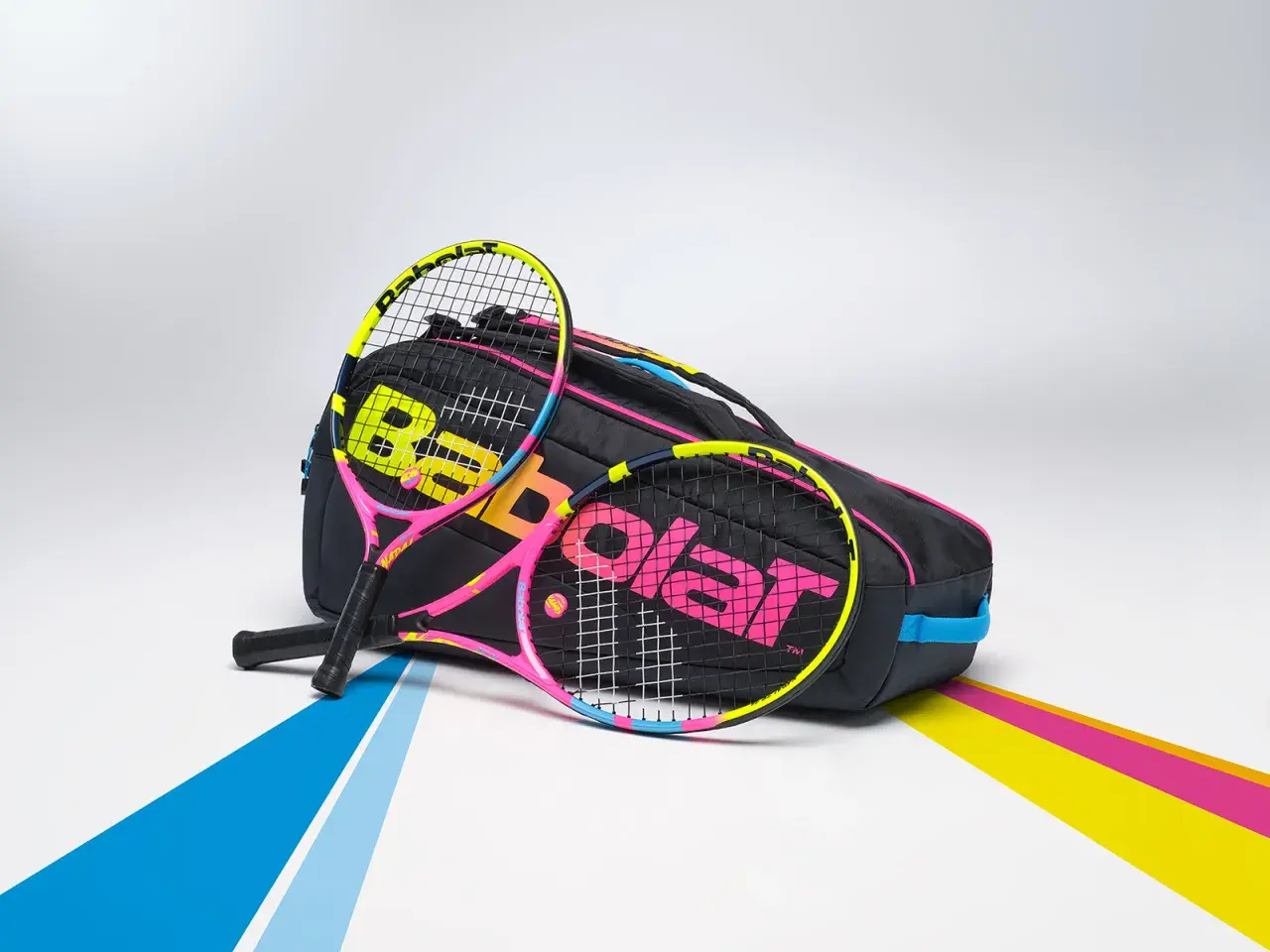 Dwie kolorowe rakiety tenisowe, jakich używałby Rafael Nadal, leżą obok czarnej torby z logo Babolat.