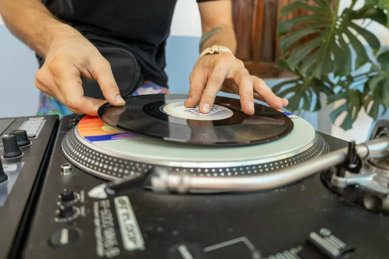 DJ kładzie winylową płytę na gramofonie. Kolorowy **cover** pod nią dodaje klimatu.