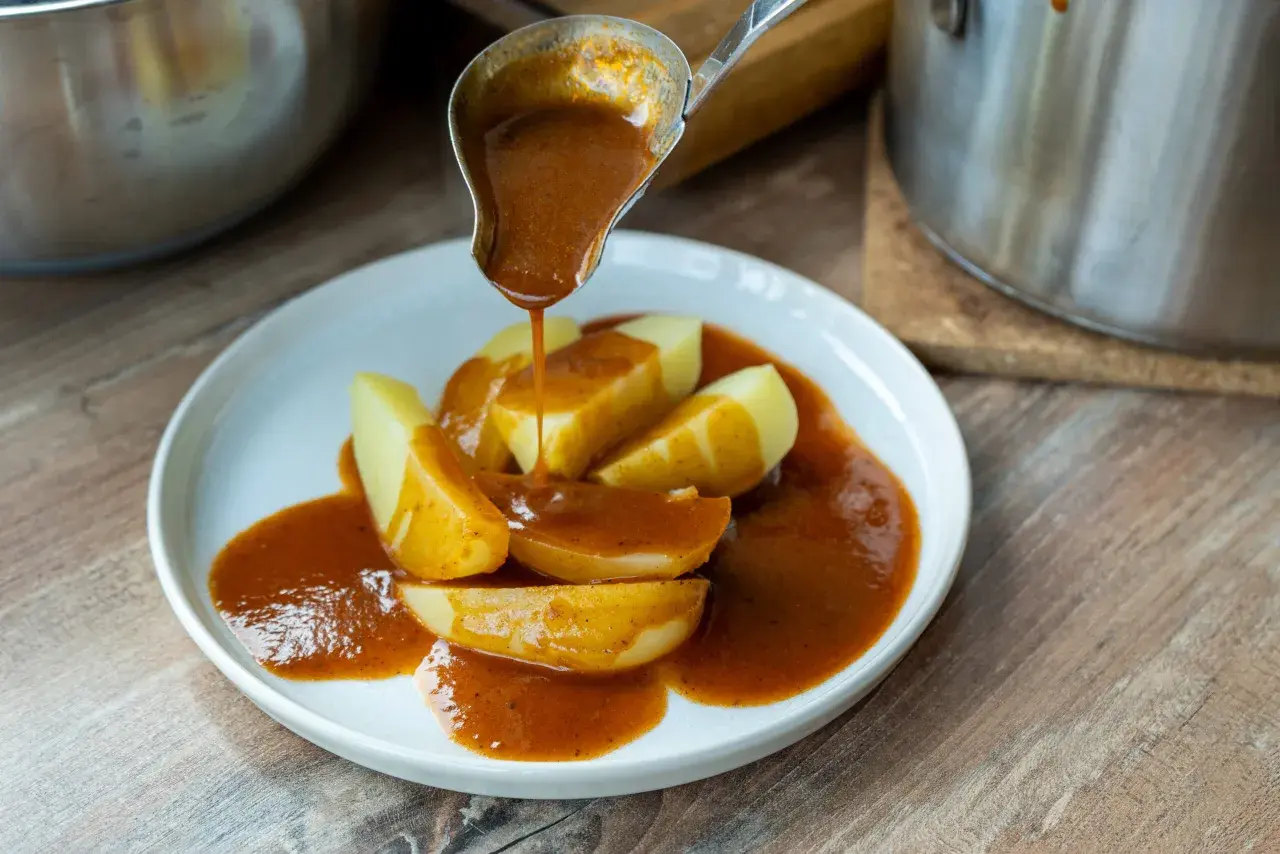 Eine Schöpfkelle gießt eine köstliche braune Sauce über Kartoffelspalten auf einem Teller.