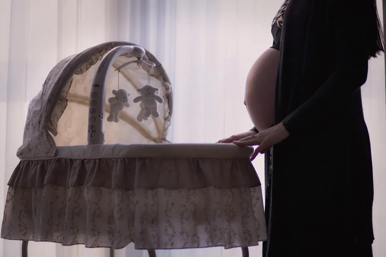 Gravid kvinna med ruckbart huvud vid en vagga med nallar.