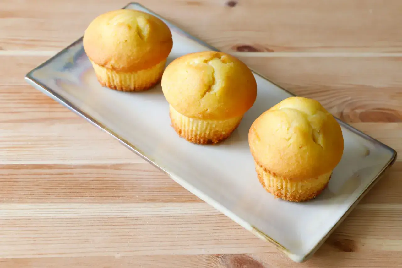 Tre soffici muffin allo yogurt dorati, serviti su un piatto rettangolare su un tavolo di legno.