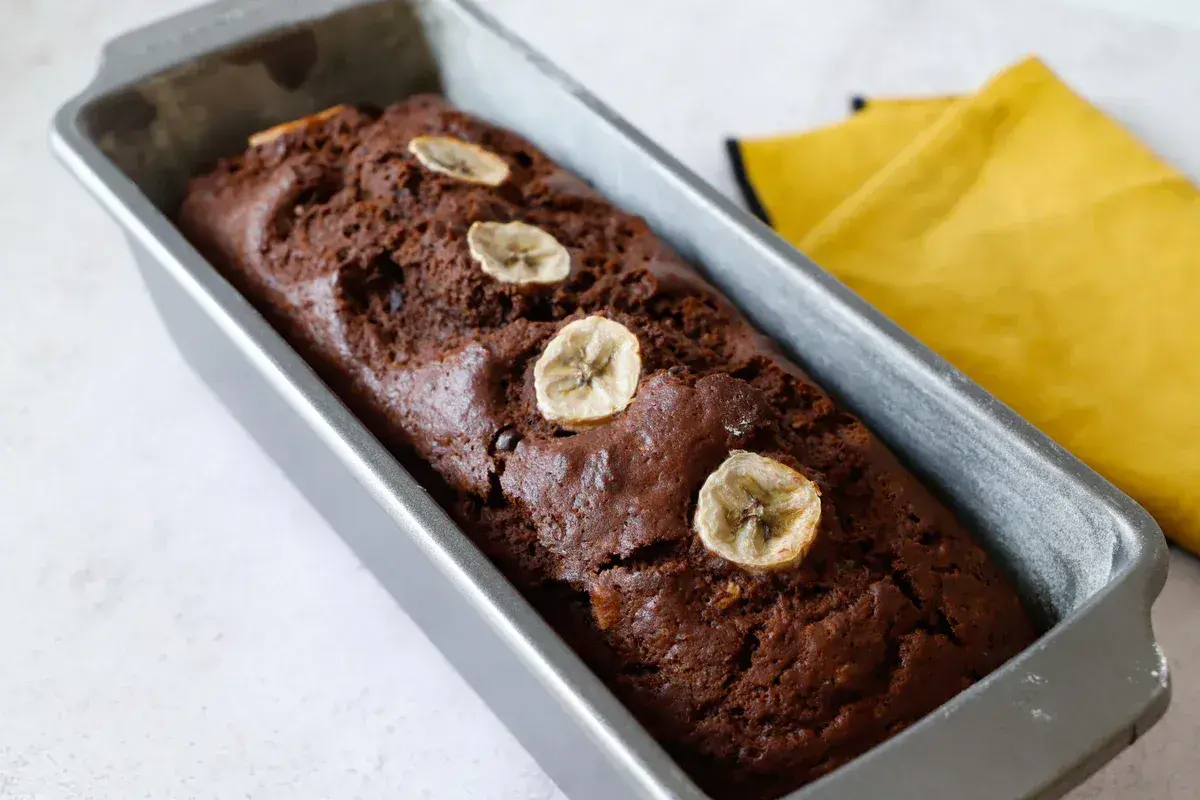 Plumcake banana e cioccolato appena sfornato, decorato con fettine di banana essiccata, in uno stampo metallico.