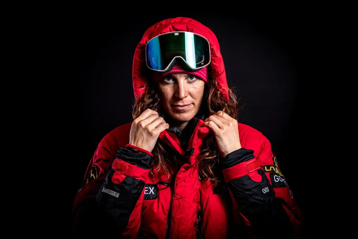 Tamara Lunger, bereit für extreme Bedingungen, zieht ihre rote Kapuze hoch. Ihre Skibrille spiegelt das Licht.