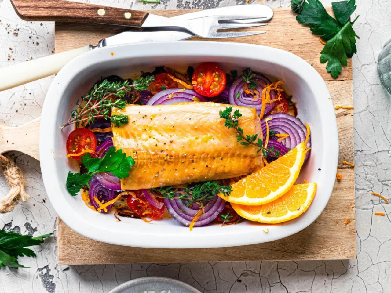 Saftiger Kabeljau im Ofen mit roten Zwiebeln, Tomaten, Kräutern und Orangenscheiben.