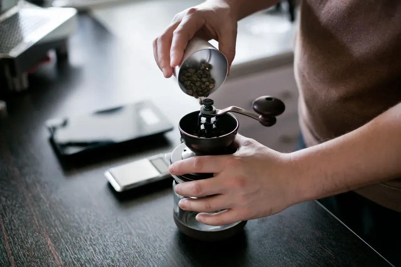 Mani versano chicchi di caffè in un macinino manuale, iniziando la macinazione per un caffè perfetto.
