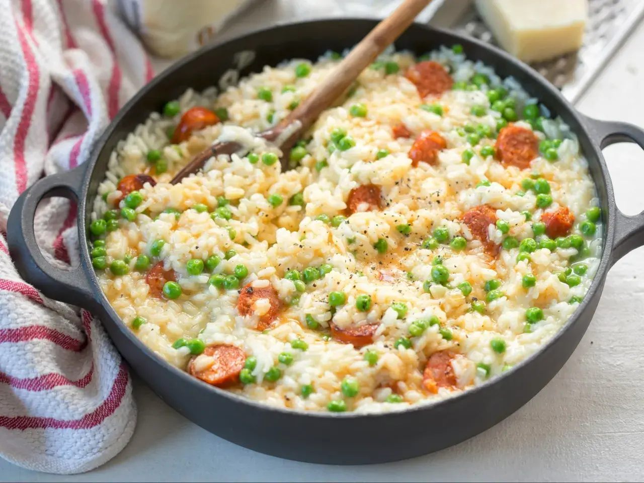Pyszne risotto z kiełbasą i groszkiem, podane w czarnej patelni, z drewnianą łyżką.