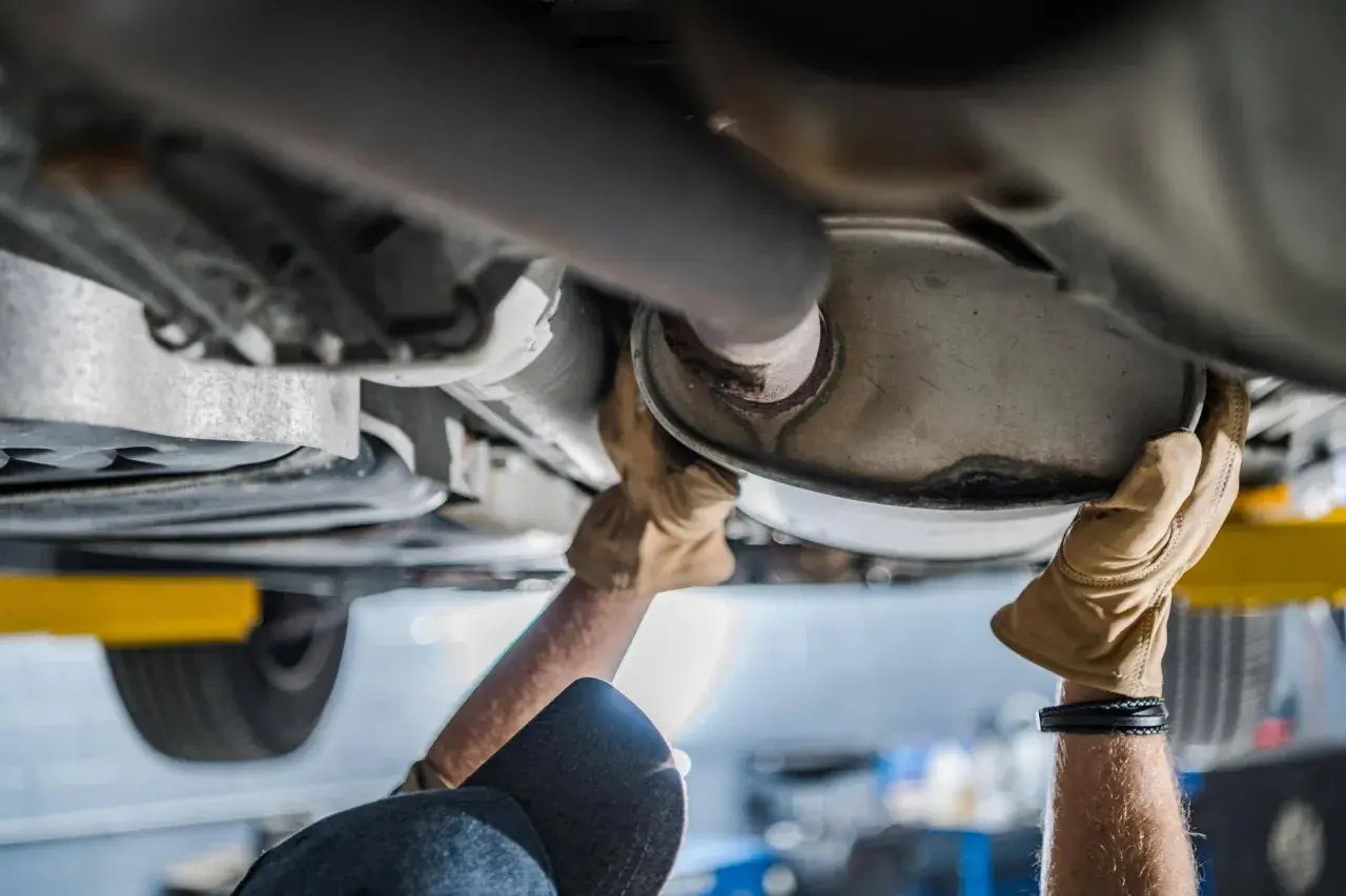 Mani guantate lavorano sul sistema di scarico, forse sostituendo il catalizzatore auto.