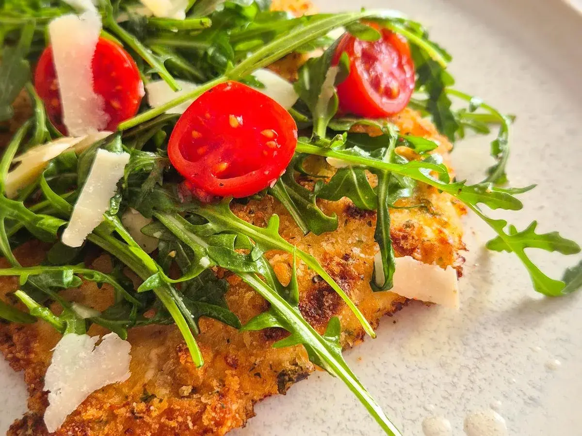 Knuspriges paniertes Hähnchen mit Rucola, Kirschtomaten und Parmesan.