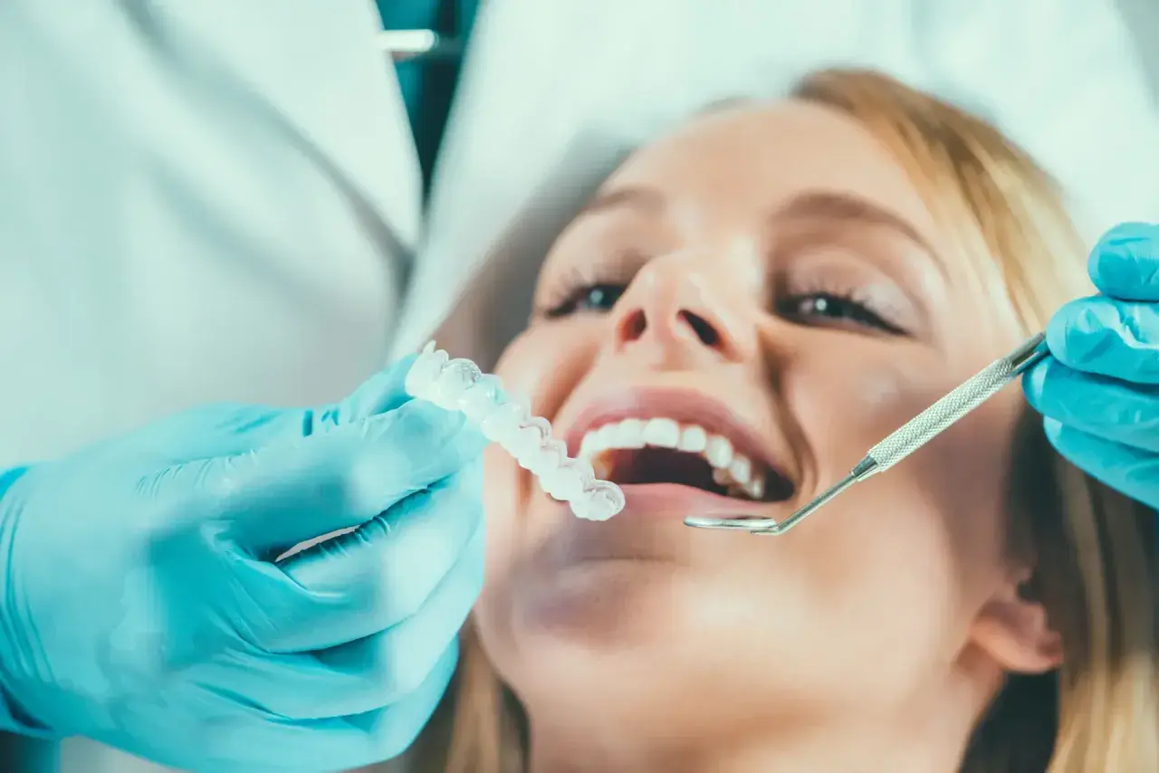 Dentysta w niebieskich rękawiczkach pokazuje pacjentce przezroczystą szynoprotezę.