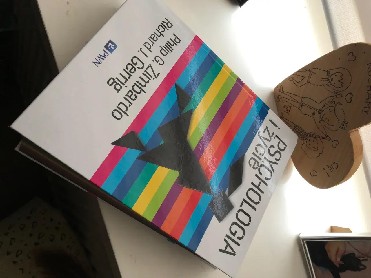Na biurku leży książka "Psychologia" autorstwa Philipa G. Zimbardo i Richarda J. Gerriga, obok drewniane serce z rysunkami.