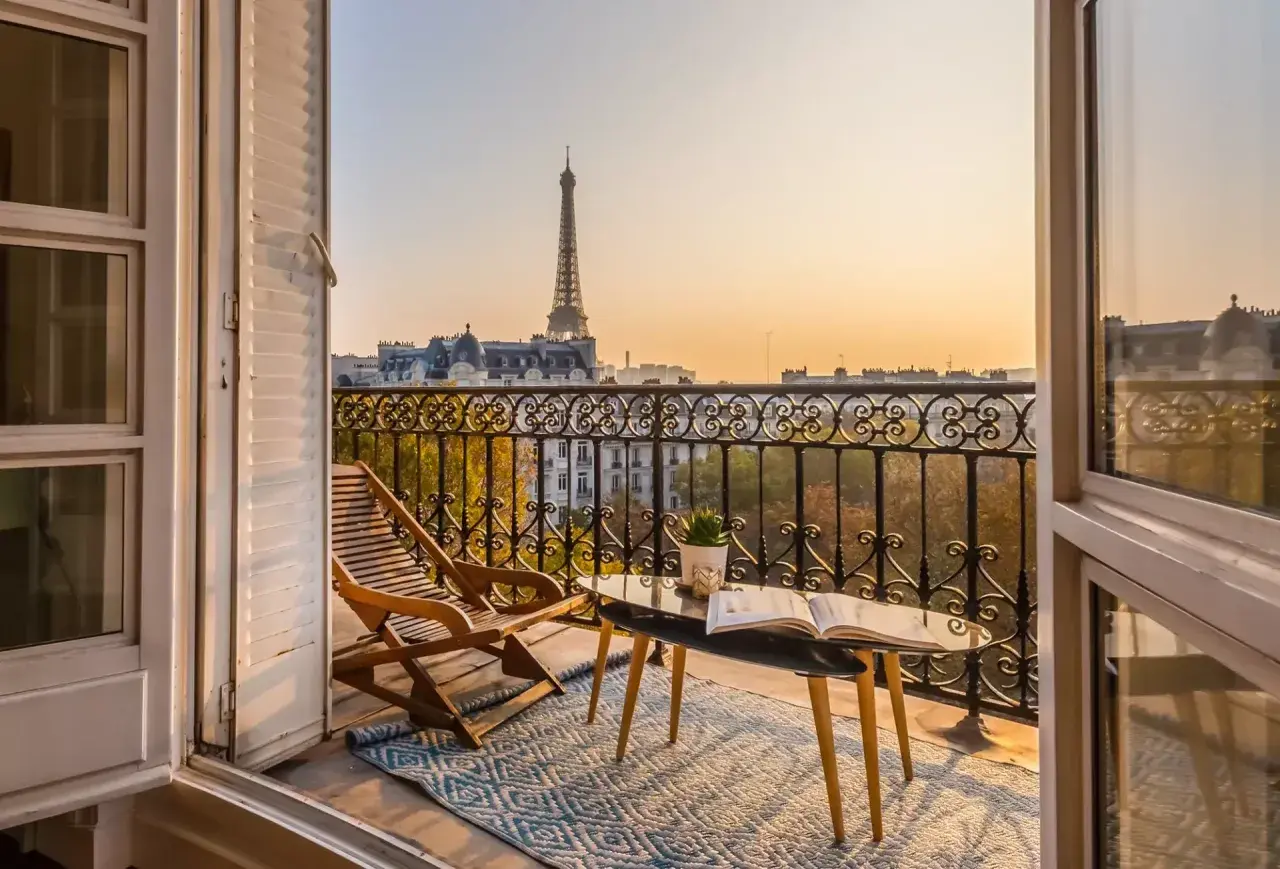 Balkon mit Blick auf den Eiffelturm, ideal für eine Reise von Zürich nach Paris. Ein Buch und ein Liegestuhl laden zum Entspannen ein.