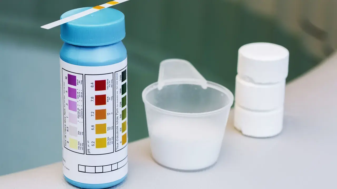Teststreifen für den ph-wert pool, daneben ein Messbecher mit weißem Pulver und Tabletten.