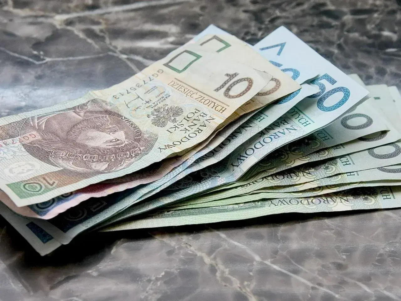Złotówki na marmurowym tle. Myśląc o przyszłości, warto rozważyć rentę chorobową po 50 roku życia.