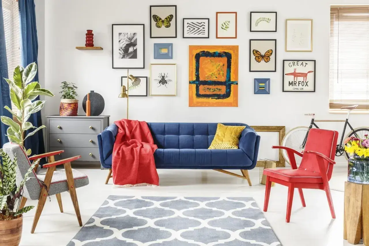 Salon w stylu eklektycznym: granatowa kanapa, czerwone fotele, galeria obrazów z motylami i owadami, szara komoda, dywan z geometrycznym wzorem.
