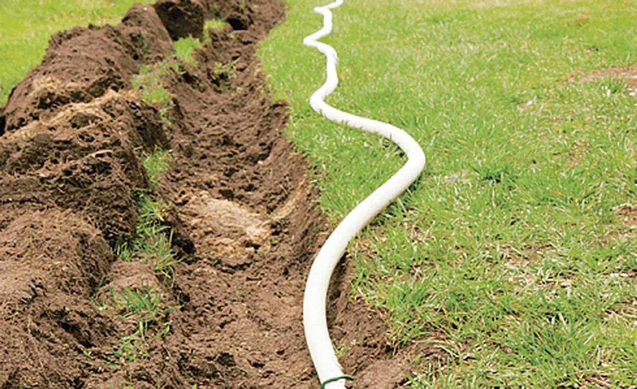 Ein Graben wird für das Erdkabel verlegen vorbereitet. Ein weißes Kabel schlängelt sich über das Gras neben dem aufgeworfenen Erdreich.