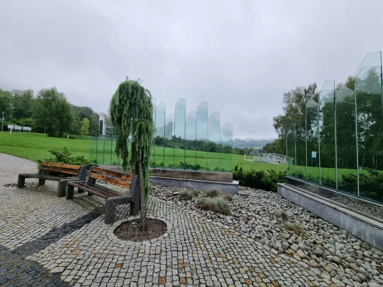 Ławki i ozdobne drzewko w Ustroniu, idealne na deszczowe atrakcje. Szklane panele tworzą nowoczesną instalację.