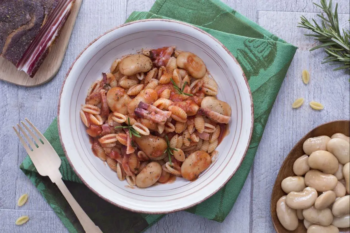 Gnocchetti alla sarda con fagioloni, pancetta y salsa de tomate, decorado con romero.