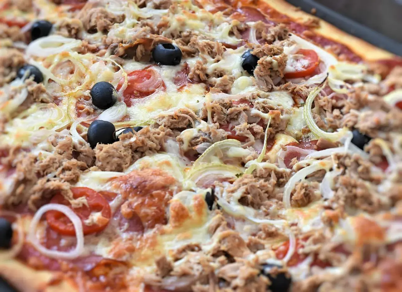Pyszna pizza z tuńczykiem, oliwkami, cebulą i pomidorami, obficie posypana serem. Idealna na szybki obiad.
