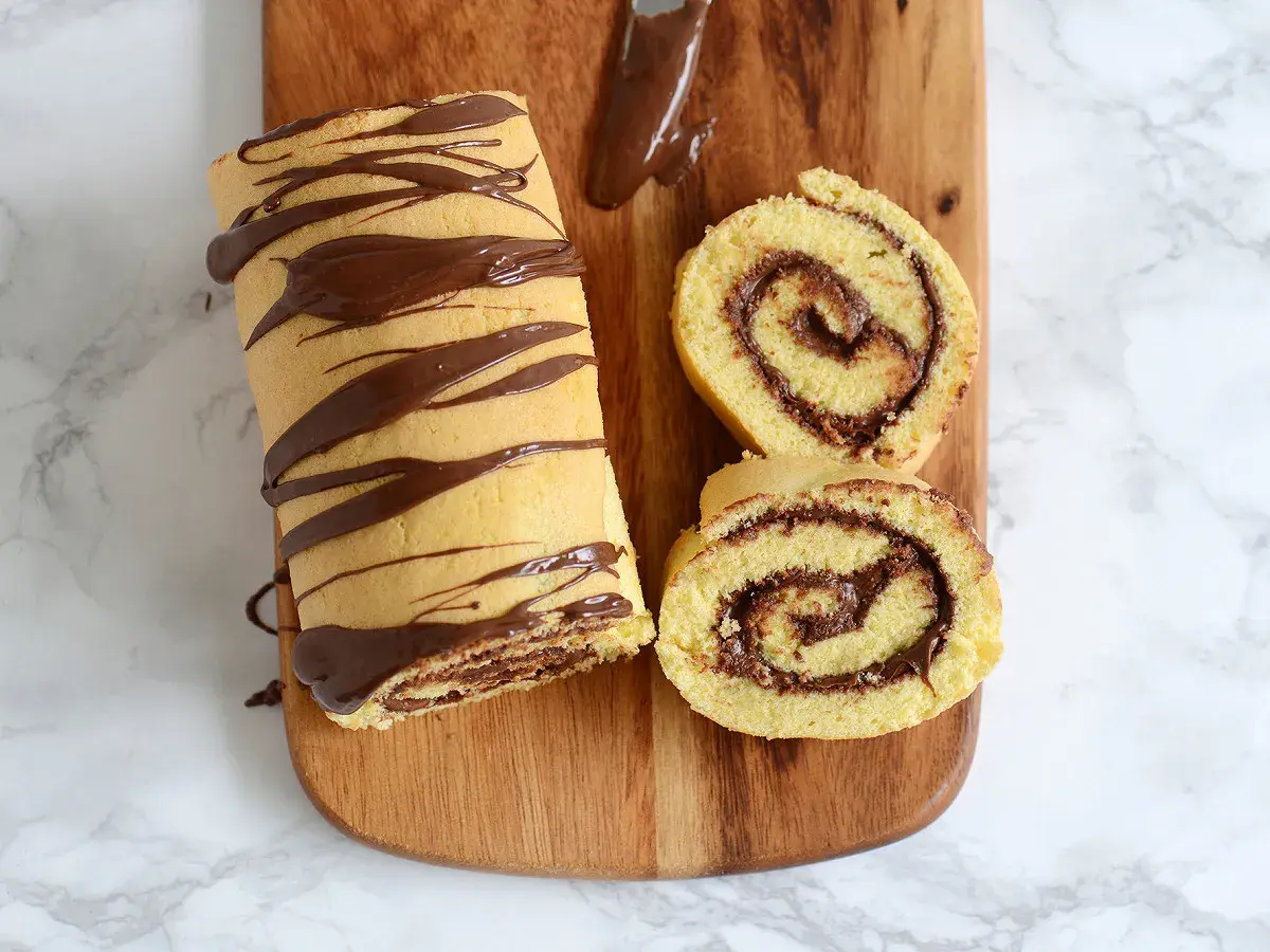 Un roulé au Nutella, entier et tranché, décoré de chocolat fondu sur une planche en bois. Un délice gourmand !