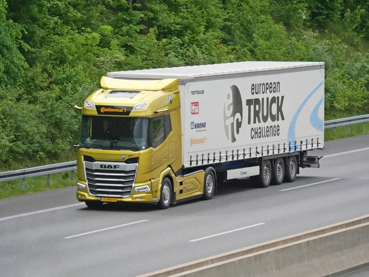 Un camion jaune DAF XF participe au European Truck Challenge, sur une autoroute bordée d'arbres.
