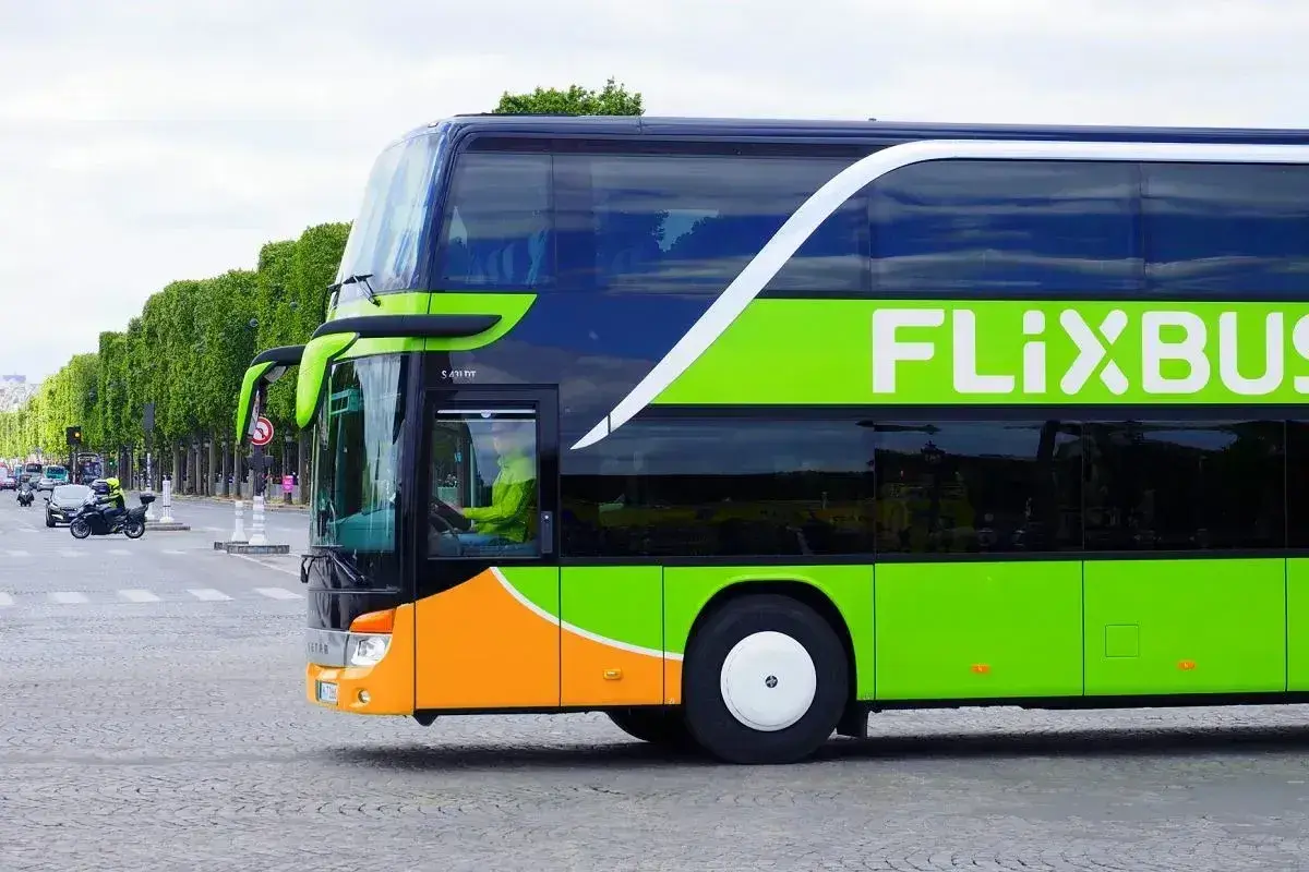 Zielony autokar FlixBus jedzie ulicą. Kierowca w żółtej kurtce prowadzi pojazd. Czy FlixBus robi postoje? Tak, ten autokar na pewno zatrzymuje się na trasie.