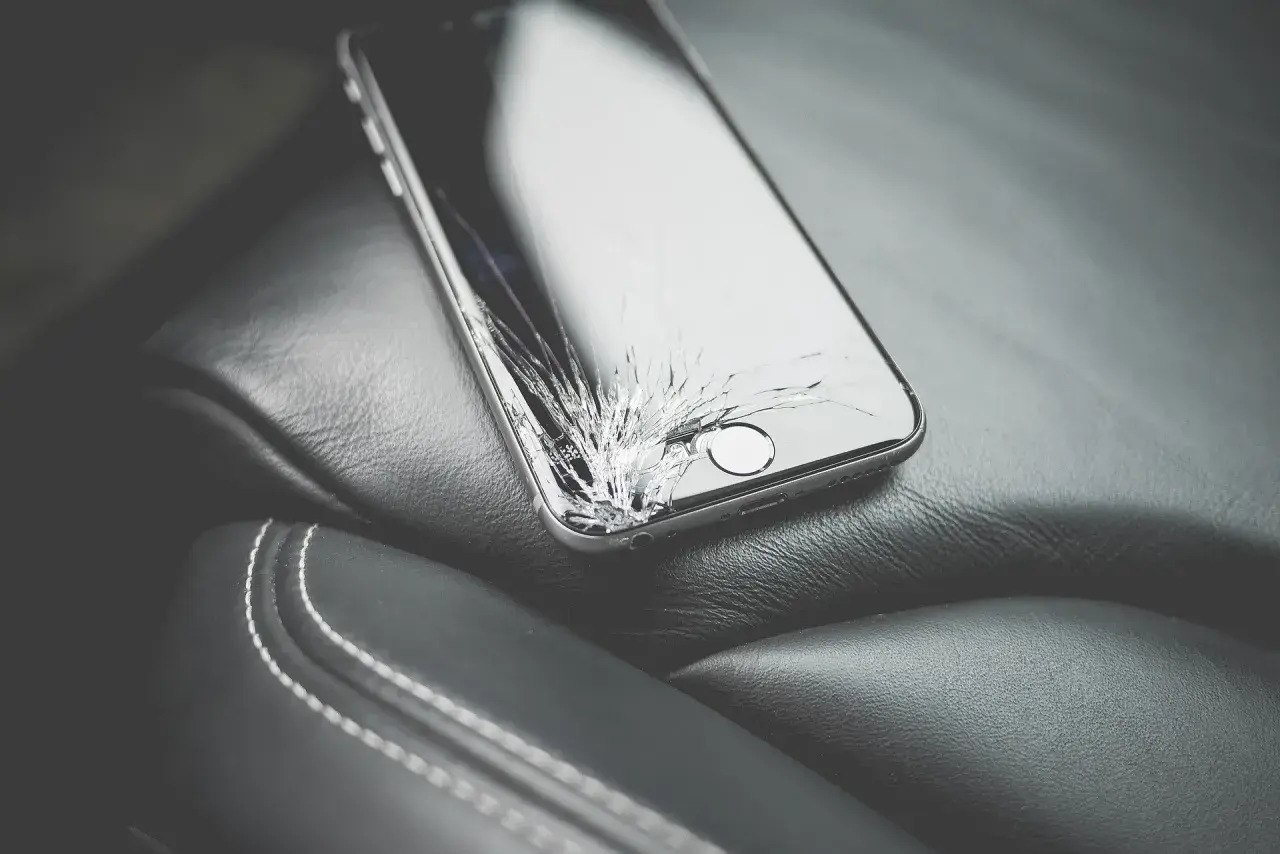 Uszkodzony ekran telefonu leżący na skórzanym siedzeniu.