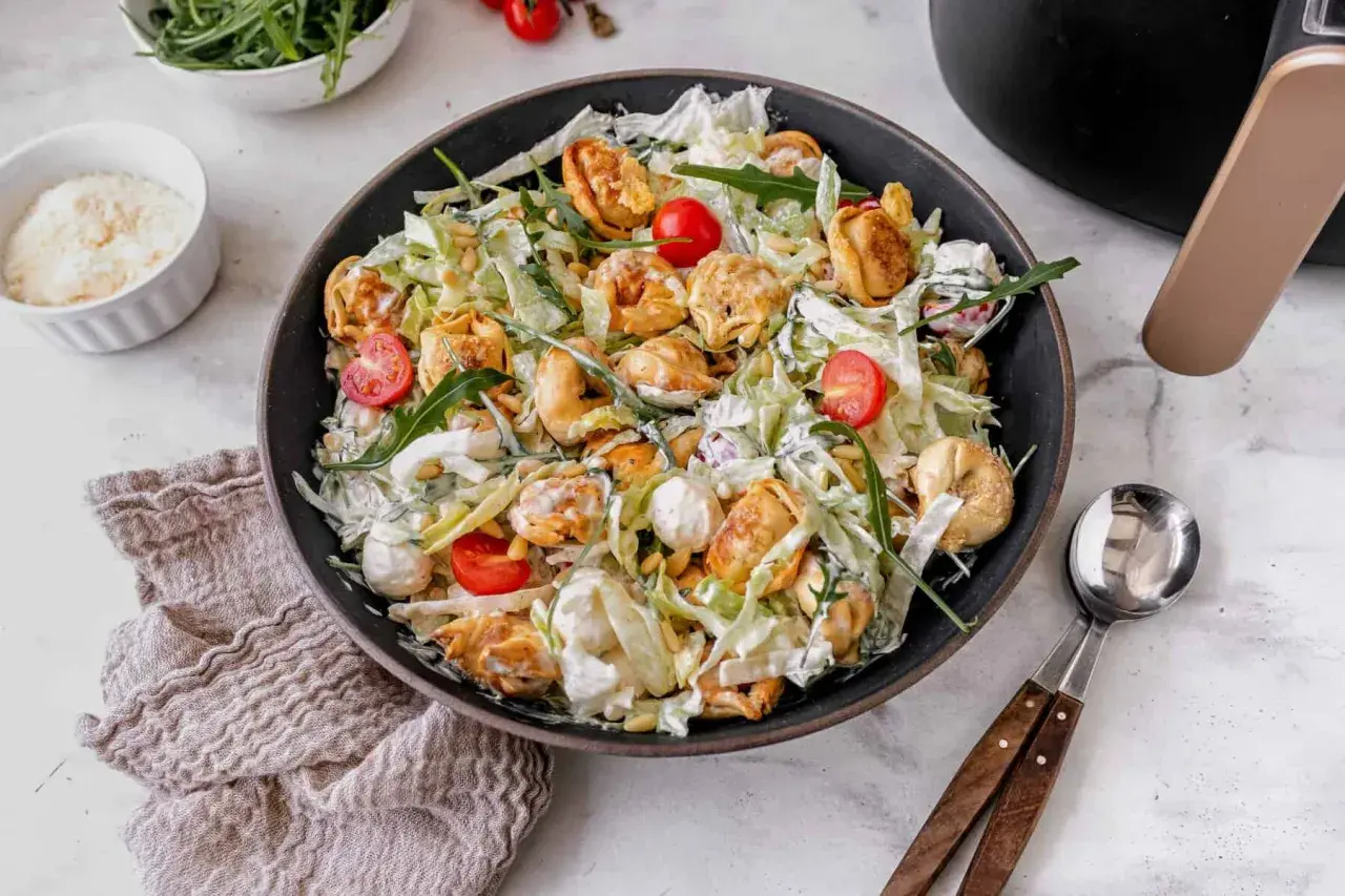 Ein üppiger italienischer Salat mit Tortellini, Kirschtomaten, Rucola und Pinienkernen, übergossen mit einer cremigen Sauce.