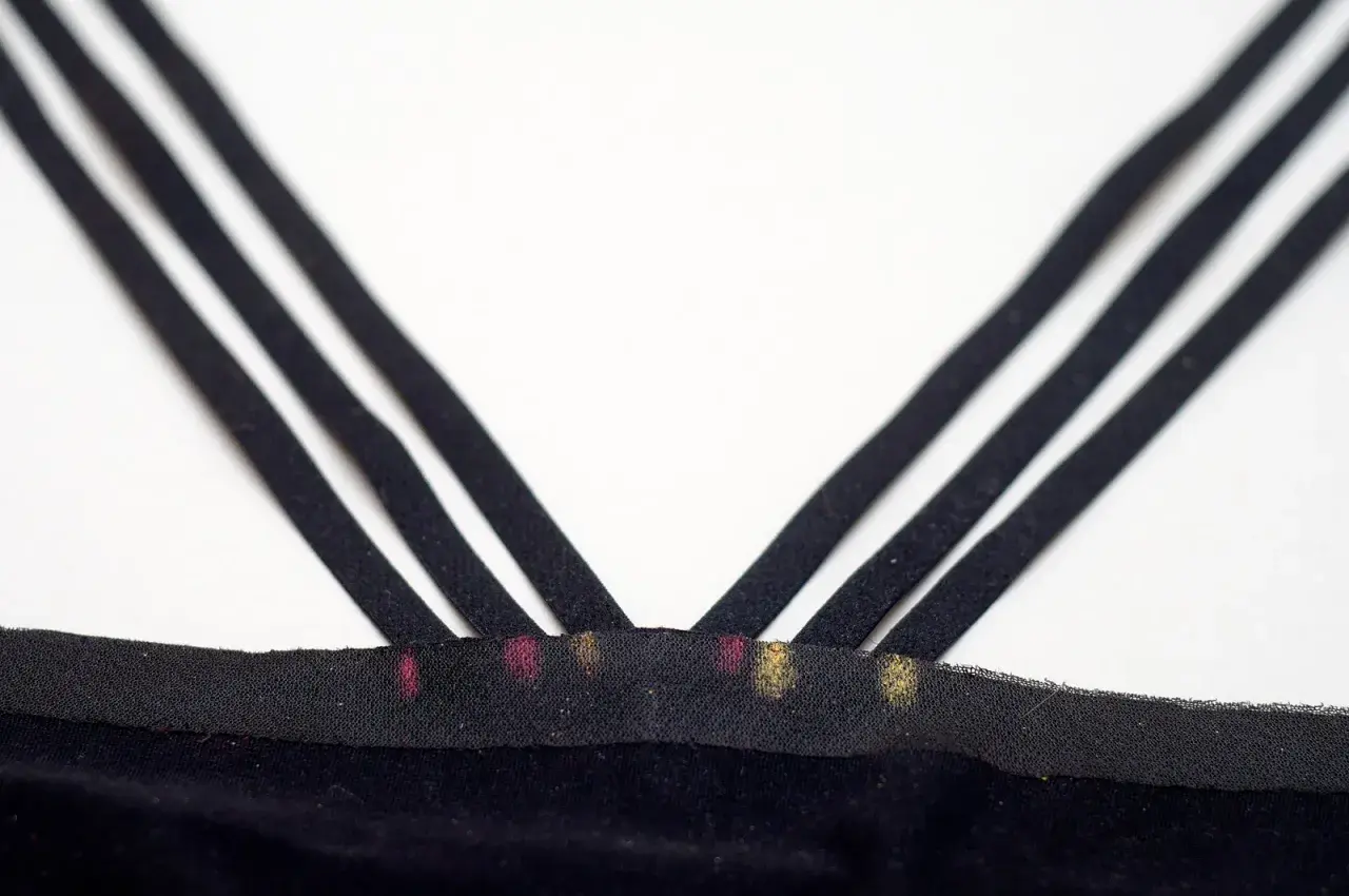 Close-up of three black bra straps crisscrossing over a black fabric band with pink and gold marks.