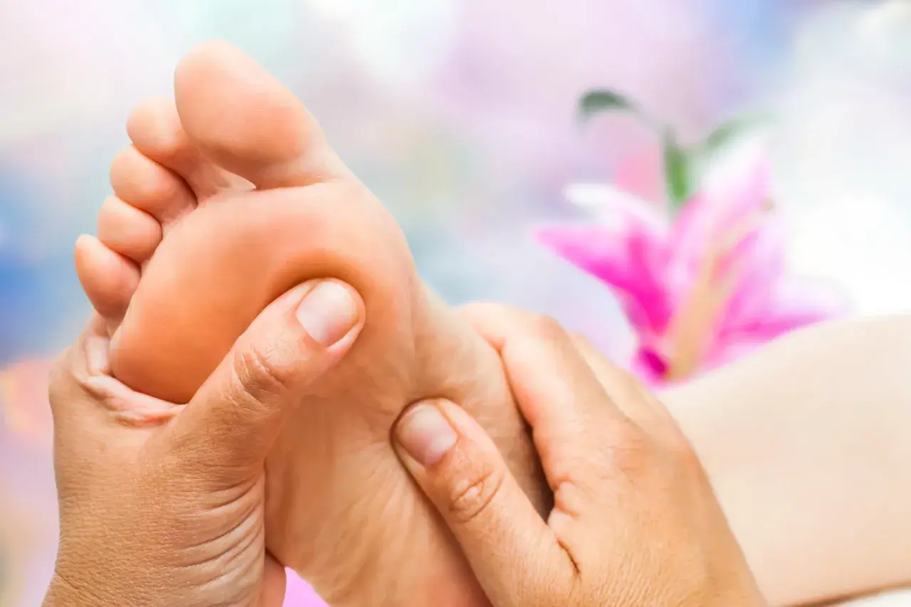 Close-up of hands massaging a foot with a blurred pink flower in the background.