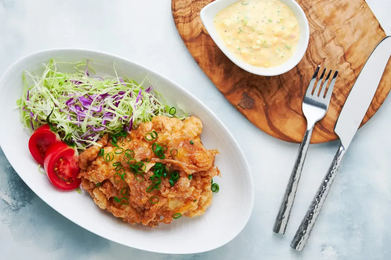 Crispy nanban food, a delicious fried chicken dish, served with shredded cabbage, tomato slices, and a creamy tartar sauce.