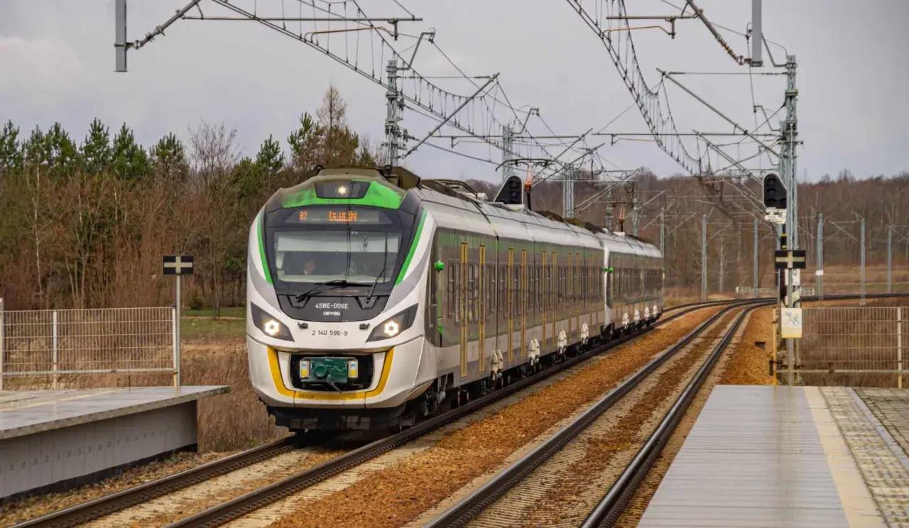 Nowoczesny pociąg 45WE-006E z zielonymi akcentami mija peron, gotowy do dalszej podróży.