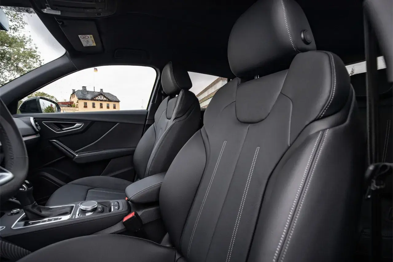 Interni Audi Q2: sedili in pelle nera con cuciture a contrasto, cambio automatico e un edificio storico sullo sfondo.