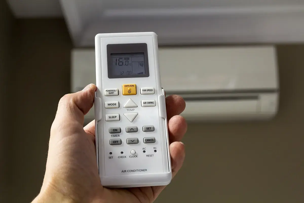Mano sujetando control remoto de aire acondicionado, mostrando 16°C. La "A" en el aire acondicionado podría indicar modo automático o alguna función específica.