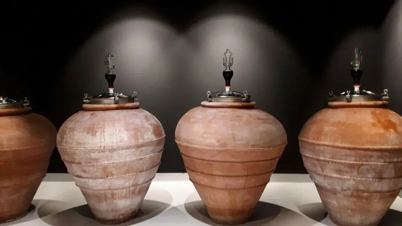 Quattro anfore in terracotta, con tappi metallici e gorgogliatori, pronte per la fermentazione del vino.