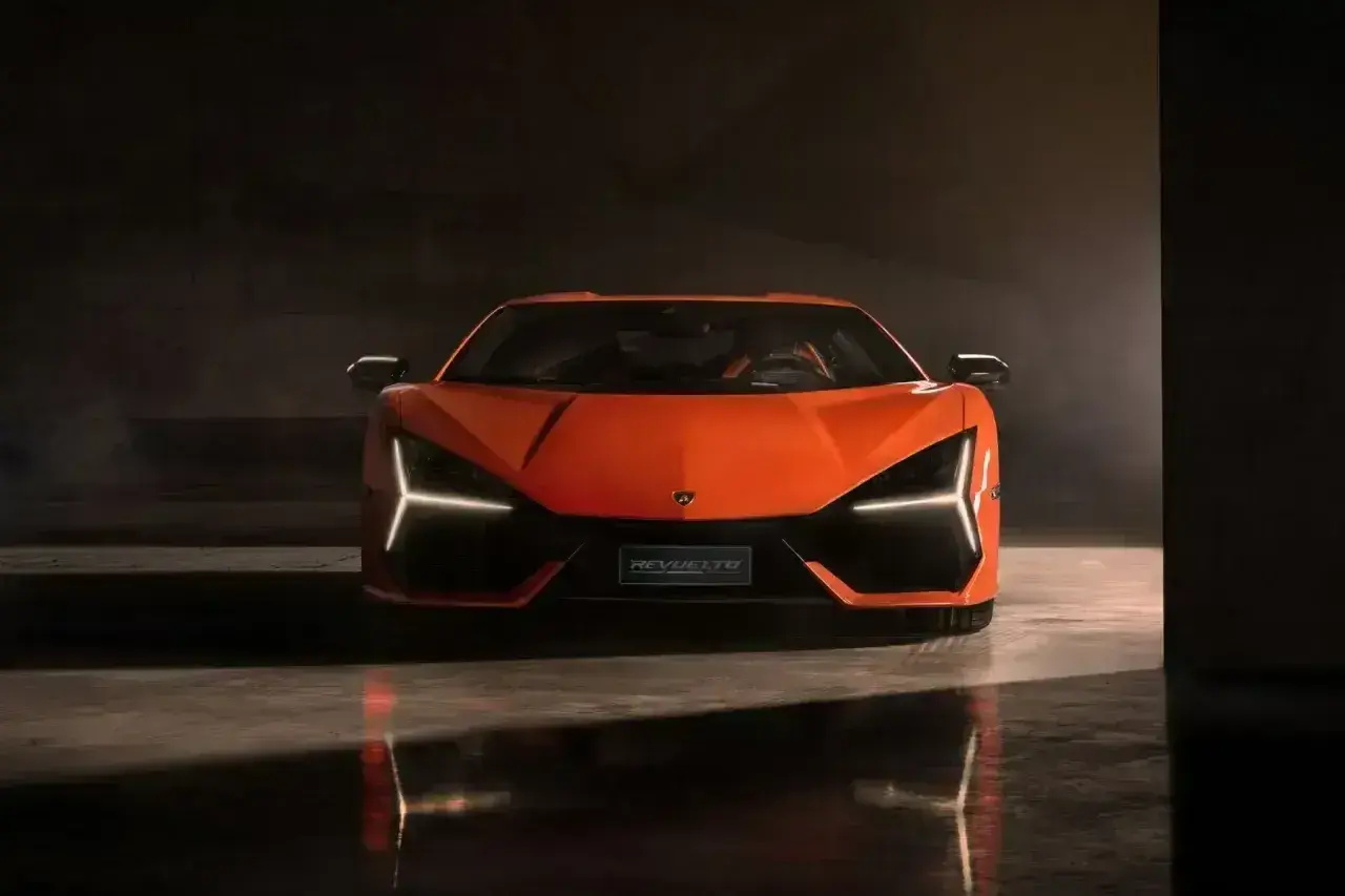 Pomarańczowy Lamborghini Revuelto z ostrymi światłami LED, odbijający się w mokrej podłodze.