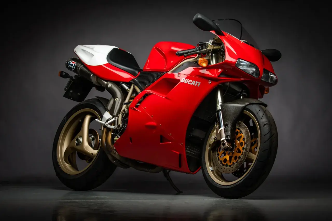 Czerwony motocykl Ducati z białym siedzeniem i złotymi felgami na ciemnym tle.