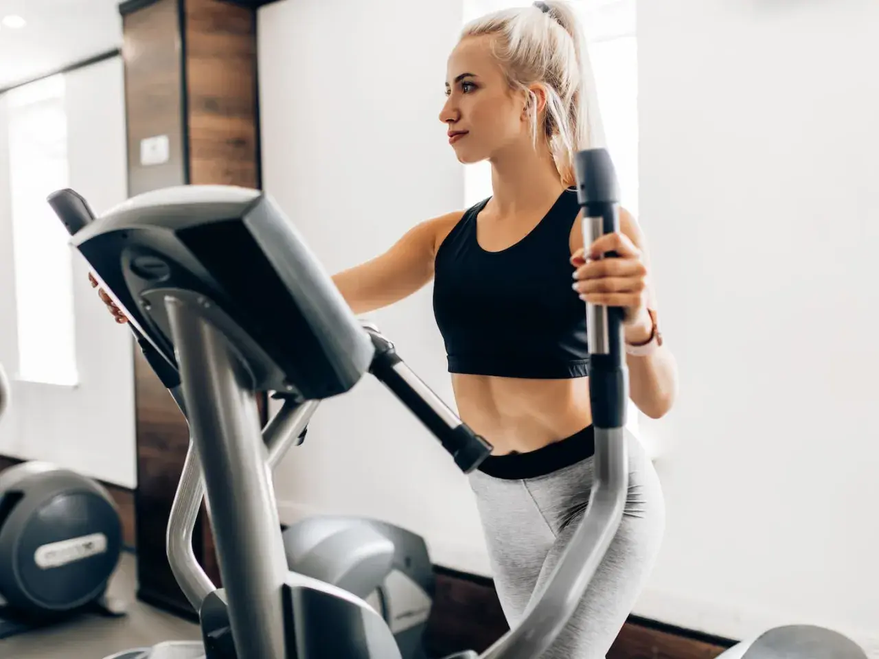 Junge Frau trainiert auf Crosstrainer, um ihren Kalorienverbrauch zu steigern.