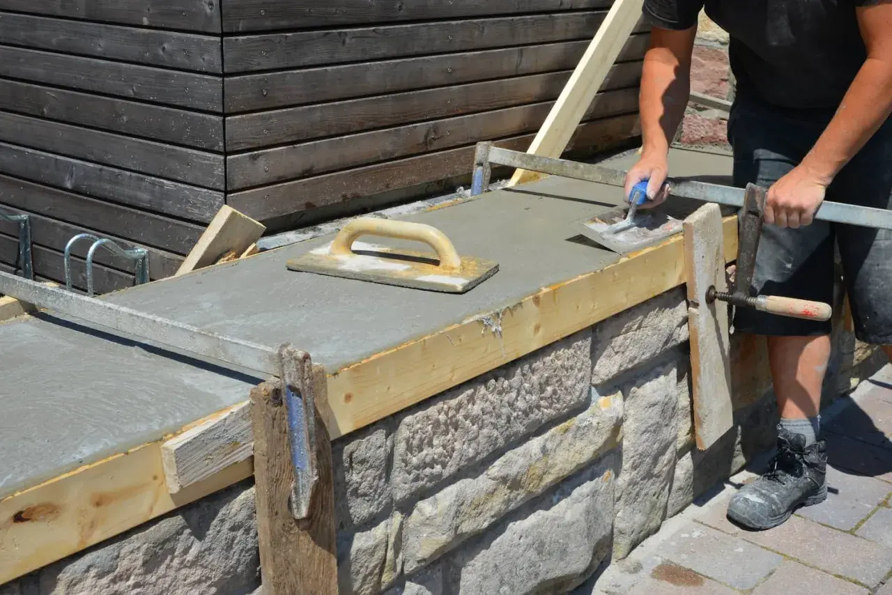 Arbeiter glättet frischen Beton auf einer **Wandschalung**. Der Aufbau der Schalung aus Holz und Metall ist gut sichtbar.