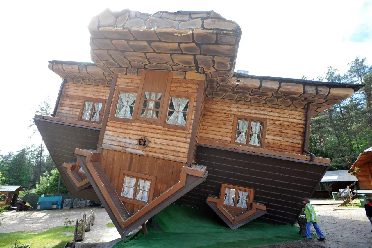 Niezwykłe, ciekawe budowle - dom do góry nogami, z dachem na ziemi i fundamentami w niebo. Dzieci podziwiają tę iluzję.