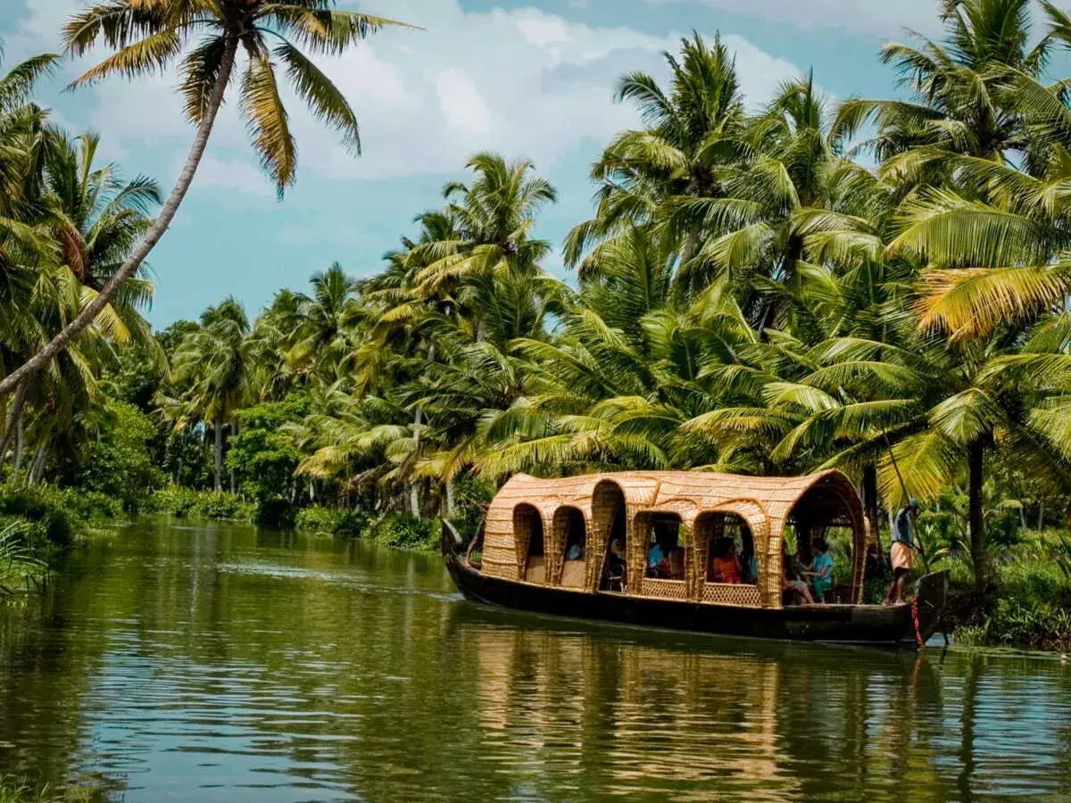 Une péniche navigue sur un canal bordé de palmiers luxuriants. Une belle façon de découvrir que faire au Kerala.