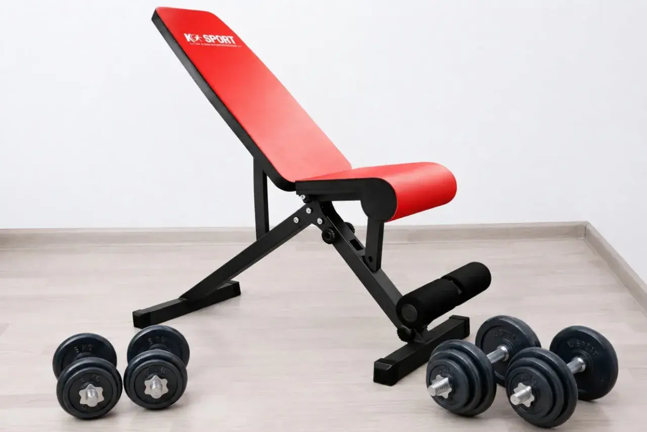 Rote Hantelbank mit schwarzem Rahmen und Hanteln auf dem Boden. Perfekt für dein Home-Gym, die beste Hantelbank für dein Training.