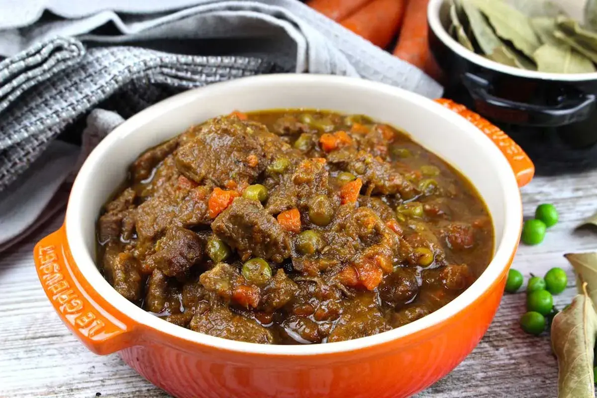 Ternera a la jardinera en un cuenco naranja, con trozos de carne tierna, guisantes y zanahoria en una rica salsa.