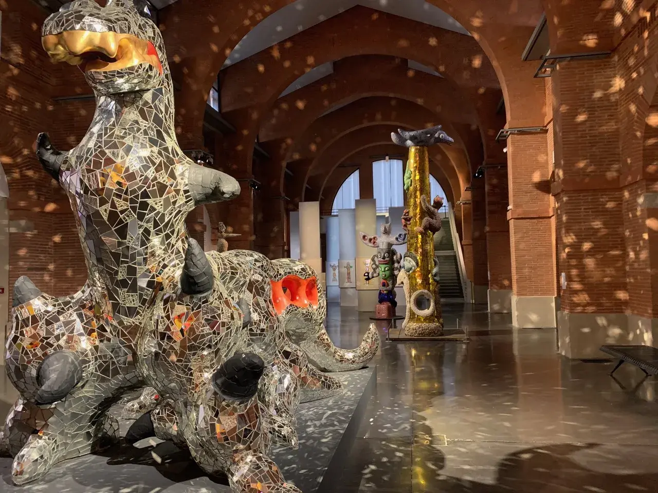 Sculptures de Niki de Saint Phalle, dont un dragon miroitant, dans un musée aux arches de briques.