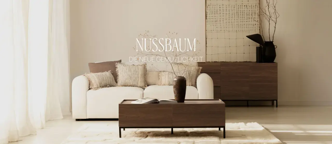Gemütliches Wohnzimmer mit weißem Sofa, Kissen und einem Couchtisch aus dunklem Holz. Ein Sideboard aus dunklem Holz steht im Hintergrund.