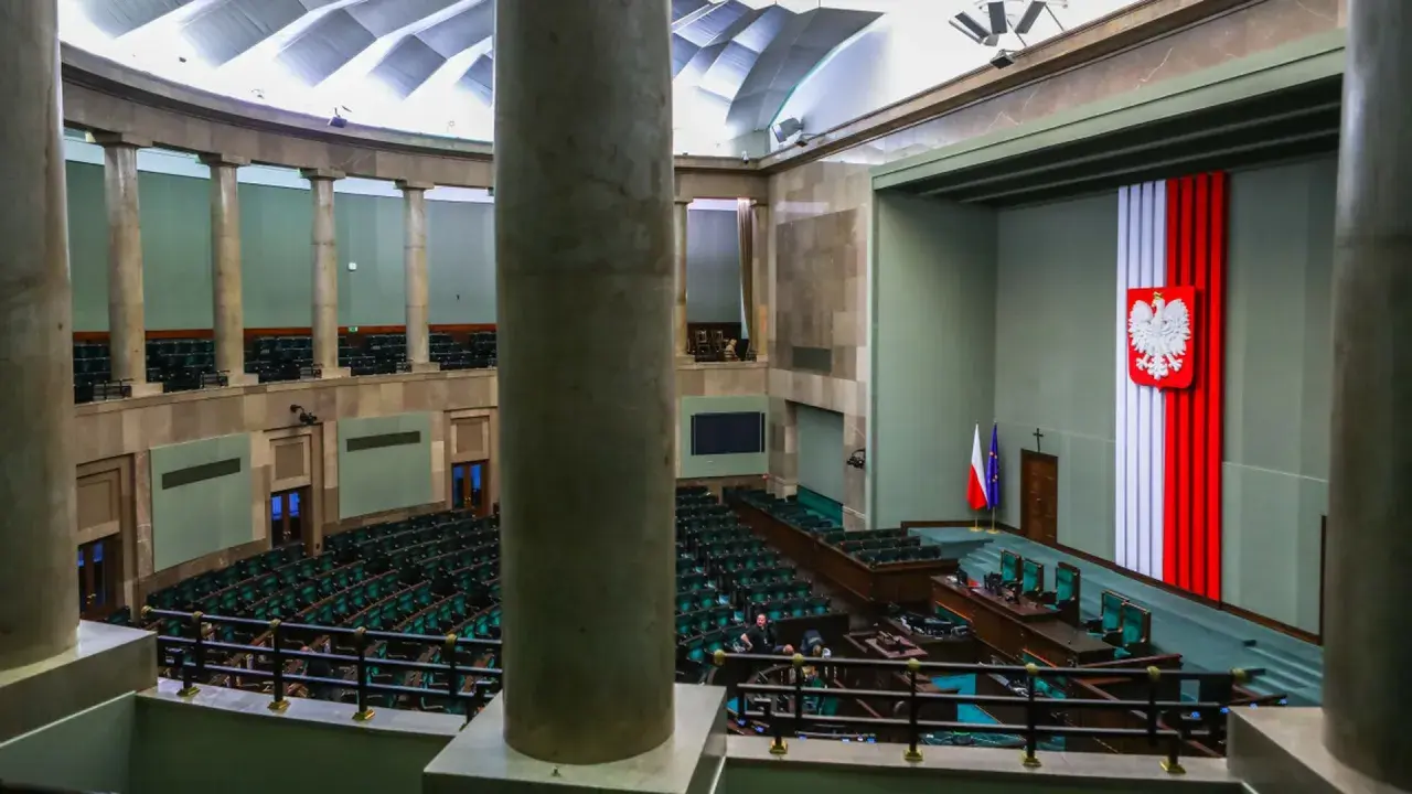 Sala sejmowa z rzędem zielonych foteli. Na ścianie godło Polski i flagi. Kto to lobbysta? Ktoś, kto próbuje wpływać na decyzje.