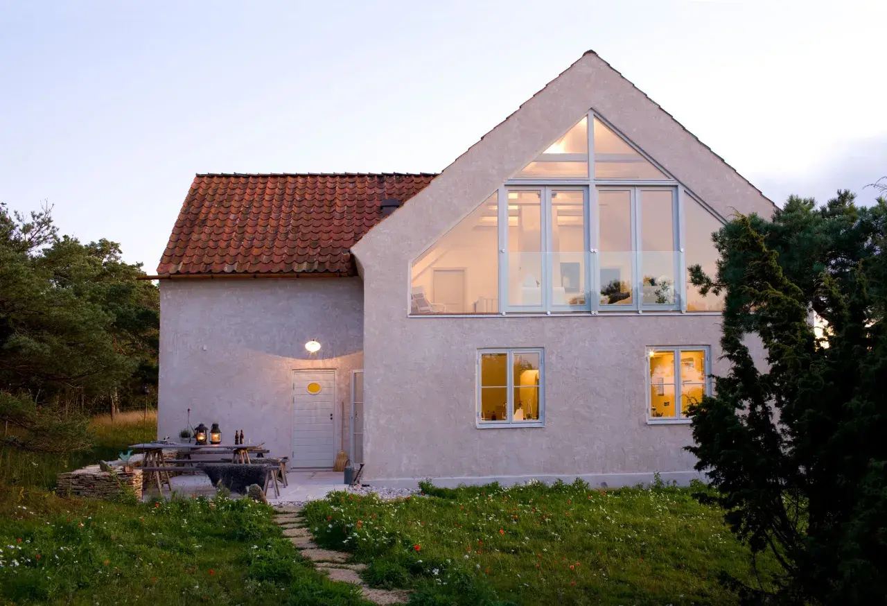 Ett modernt hus med stora fönster och en takkupa, omgivet av grönska. En uteplats med bord och stolar. Detta hus har en bra energideklaration.