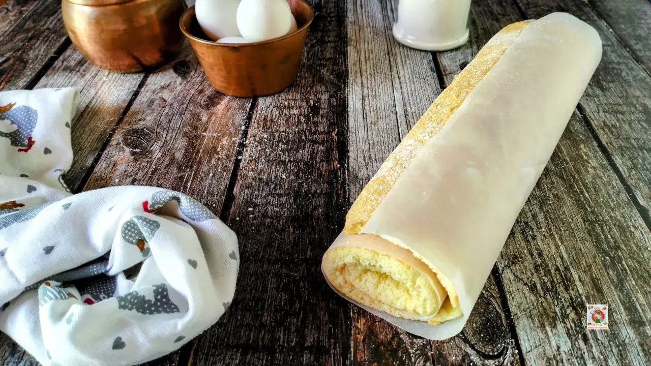 Rotolo di pasta biscotto perfetta, soffice e dorata, avvolta in carta forno. Ingredienti freschi in primo piano.