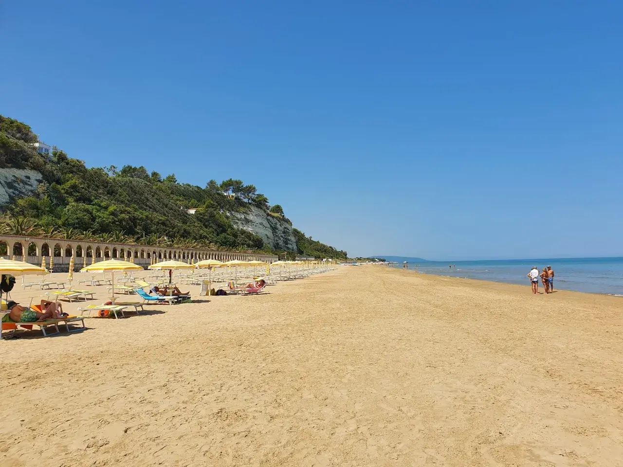 Spiaggia di ponente Rodi Garganico: sabbia dorata, ombrelloni gialli e un mare azzurro sotto un cielo limpido.